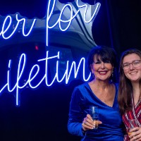 Girl in red dress and President Mantella stand in front of Laker for a Lifetime neon sign